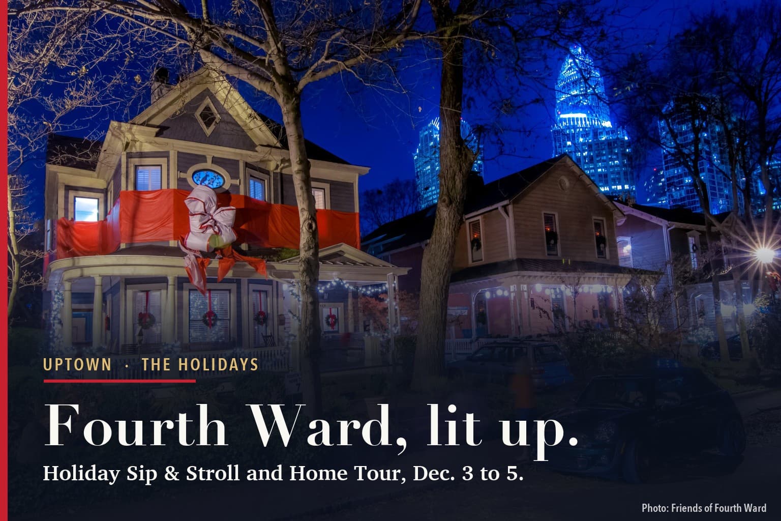 Victorian houses in Historic Fourth Ward at night, decorated for the holidays with wreaths, porch lights and a red bow wrapped around a balcony, with Uptown Charlotte towers lit blue behind them.